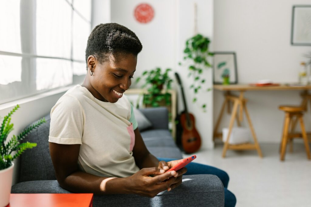 Happy young african american woman relaxing on sofa while having fun using phone